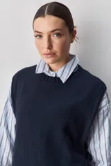 Chaleco tejido de punto color beige, con cuello redondo, terminaciones en rib y lazos laterales regulables que permiten ajustar la prenda.