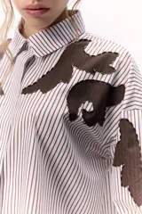 Camisa a rayas verticales blancas y marrones con bordados localizados y apliques metálicos. Tiene mangas abullonadas y cuello clásico con broche metálico.
