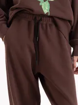 Pantalón tipo jogging de silueta amplia y largo al tobillo, confeccionado en algodón. Cuenta con cintura elastizada, cordón ajustable y bolsillos laterales. Su diseño incluye elásticos en las botamangas que permiten regular el ajuste.