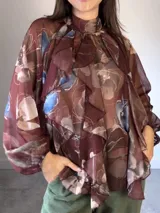 Camisa de seda italiana con estampado floral, cuello alto, mangas largas abullonadas y volados frontales. Presenta un lazo para atar en la espalda.