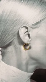 Par de aros tipo argolla pequeños, de color dorado con diseño irregular y acabado brillante.