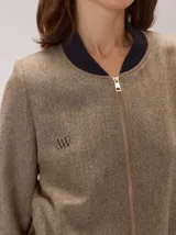 Chaqueta tipo bomber de lana con estampado de espiga en tonos grises. Presenta cuello, puños y ruedo en tejido elástico negro, cierre frontal dorado y bordado sutil en el pecho.