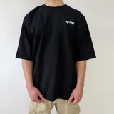 Remera negra de corte oversize con cuello redondo, manga corta y pequeño estampado en contraste en el pecho con las iniciales y la palabra 'vcp cnpt.'.