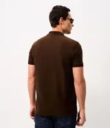 Remera polo de hombre en color marrón, confeccionada en tejido texturizado con mezcla de algodón y poliéster, de manga corta y cuello abierto sin botones.