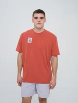 Remera Umbro de manga corta y cuello redondo, color terracota, con pequeño estampado frontal en el pecho con diseño de estampilla y logo de la marca.