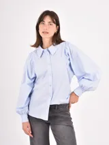 Camisa de manga larga en color celeste, con cuello clásico y cierre frontal de botones. Presenta un diseño con mangas abullonadas y puños ajustados.