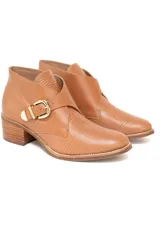 Bota corta de cuero vacuno grabado con efecto croco y terminación charolada en color ámbar. Presenta un diseño con hebilla metálica dorada lateral y taco medio fachetado con efecto madera.