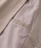 Campera bomber masculina de terciopelo cotelé color beige, con cuello redondo, mangas largas, cierre frontal de botones forrados, bolsillos laterales y terminaciones de elástico en puños y cintura.