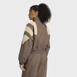Campera deportiva Adidas de corte holgado, con cierre frontal y cuello alto. Presenta un diseño en bloques de color marrón y beige, con detalles inspirados en la estética futbolística de los años 90.