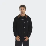 Campera estilo carpenter de color negro con cuello de pana en contraste color marrón. Presenta cierre frontal con botones metálicos, bolsillos frontales tipo parche y un pequeño parche con logo en el pecho.