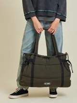 Bolso tipo tote bag de diseño acolchado en color verde militar. Cuenta con correas de hombro resistentes, cierres laterales ajustables con cordones y un parche con el logo de la marca en la parte inferior frontal.