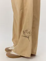 Pantalon ancho de lino color beige, de corte holgado y fluido, con detalle de bordado floral en la parte inferior de la pierna.