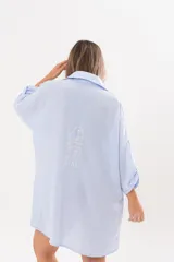 Vestido camisero de lino color celeste, con escote en V, cuello clásico, cierre frontal de botones y mangas tres cuartos regulables. Diseño holgado con corte asimétrico.
