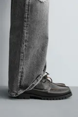 Zapato náutico de cordones, color negro, fabricado en piel con pespuntes a contraste en color claro. Presenta una horma redonda y suela track gruesa.