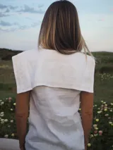 Blusa sin mangas de lino color blanco, con cuello marinero grande y detalles de encaje en el cuello y a lo largo de la botonadura frontal.