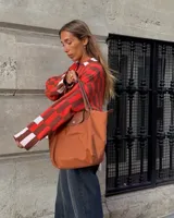 Saco tejido de punto con diseño de cuadros en tonos rojo, marrón y rosa claro. Presenta corte recto oversize, cierre frontal con botones en forma de corazón y dos bolsillos delanteros.