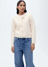 Chaqueta de punto calado en color crema, con cuello redondo, manga larga y cierre frontal mediante botones dorados. Presenta un diseño recto y tejido de punto medio.