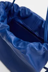Bandolera mini de piel color azul, con doble asa fina, detalle de pespunte central y cierre mediante fruncido. Cuenta con un bolsillo interior.