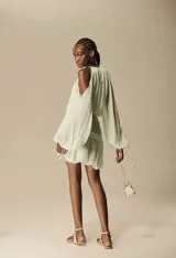 Vestido corto color verde menta claro, con escote halter y hombros descubiertos. Presenta mangas largas amplias y ajustadas en el puño, y un corte fruncido en la cintura que da lugar a una falda corta con volados.