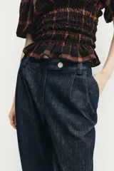 Pantalón chino de tiro medio confeccionado en denim oscuro. Presenta pinzas en el delantero, bolsillos laterales y bajo con acabado en vuelta. Cierre frontal con cremallera y botón.