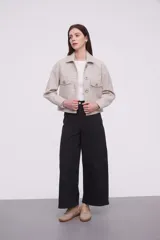 Chaqueta corta color arena melange con cuello camisero, cierre frontal con botones dorados y bolsillos de parche en el pecho.