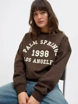 Buzo marrón de cuello redondo con estampado frontal en color blanco que dice "Palm Springs 1998 Los Angeles". De corte relajado y mangas largas con puños elásticos.