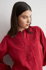 Blusa blanca de corte holgado con cuello mao y escote en V. Presenta detalles de bordado calado en el pecho y en los puños de las mangas tres cuartos.