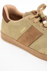 Zapatilla de gamuza en tono verde pistacho con detalles en cuero marrón, cordones al tono con cuentas decorativas y suela de goma color caramelo.
