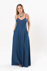 Vestido largo de denim fino y liviano, color azul, con breteles finos, escote en V y falda amplia con recortes verticales y bolsillos laterales.