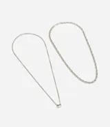 Kit de dos collares masculinos de metal con acabado plateado. El conjunto incluye una cadena de eslabones ovalados y una cadena fina con un pequeño dije central, diseñados para usar en superposición.