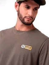 Remera de manga corta y cuello redondo en color verde oliva. Presenta un pequeño estampado rectangular en el pecho con el logo de Caterpillar y herramientas cruzadas, además de un gráfico estampado en la espalda.