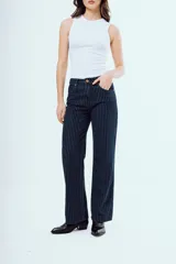 Pantalón de jean azul oscuro de corte recto y tiro medio, con diseño de rayas diplomáticas blancas. Presenta bolsillos delanteros y traseros, y cierre frontal con botón y cremallera.