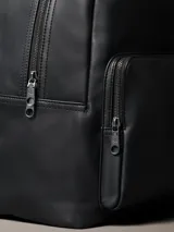 Mochila Calvin Klein de poliuretano color negro, de diseño minimalista con silueta redondeada. Cuenta con un compartimento principal con cierre, bolsillo frontal externo con cierre y el monograma CK grabado. Incluye asa superior y correas acolchadas ajustables.