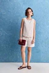 Top blanco sin mangas, con cuello redondo, diseño cruzado en el frente y cierre con botones en el hombro.