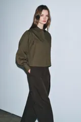 Camisa de popelín color blanco con cuello solapa, cierre frontal con botones ocultos y mangas largas abullonadas con puños estructurados.