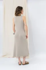 Vestido midi de tejido tipo seda con caída fluida, escote redondo y sin mangas. Presenta un diseño minimalista con detalle de flecos en el ruedo.
