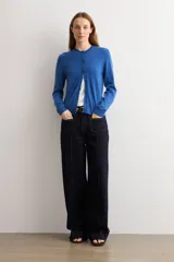 Cardigan de punto azul con cuello redondo, manga larga y cierre frontal abotonado con pequeños botones al tono.