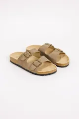 Sandalias planas estilo Birkenstock en color beige, con dos tiras ajustables mediante hebillas metálicas en tono bronce. Cuenta con plantilla anatómica y suela de corcho y goma.