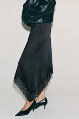 Pollera midi de punto color negro, con cintura elástica y bajo asimétrico decorado con un ribete de encaje.
