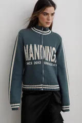Campera tejida de algodón en color rojo, con cierre frontal completo, cuello alto y puños acanalados con detalles de rayas blancas. Presenta un diseño gráfico con texto blanco en el frente.