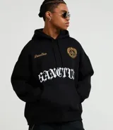 Hoodie negro de corte boxy, con capucha ajustable, bolsillo canguro y detalles bordados en el pecho. Presenta un estampado grande en la parte frontal con tipografía gótica y texto en dorado.