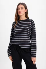 Remera de manga larga con diseño oversize, confeccionada en tejido de punto grueso a rayas horizontales en tonos marrón y blanco. Presenta cuello redondo y un pequeño bordado distintivo en el pecho.