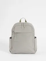 Mochila mediana de tela color gris, con compartimento principal con cierre, bolsillo frontal con cierre y bolsillos laterales abiertos. Incluye manija superior y correas ajustables.