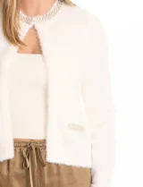 Chaqueta corta de tejido tipo mohair en color blanco, con cuello a la base decorado con bordado de perlas y canutillos. Presenta bolsillos simulados en el frente con apliques de brillos y cierre mediante broche interno.