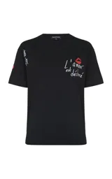 Remera negra de algodón con cuello redondo y mangas cortas. Presenta un bordado frontal con la frase 'L'amour est déclaré' acompañada de un diseño de labios rojos, y un detalle bordado adicional en la manga derecha.