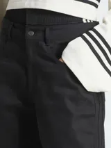 Pantalón utilitario negro de corte holgado y tejido de sarga suave, con múltiples bolsillos y tres rayas verticales en los laterales.