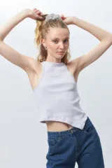 Top de algodón blanco sin mangas con cuello halter y bajo asimétrico en punta diagonal. Presenta un tejido de punto acanalado y un diseño inspirado en la estética de los años 2000.