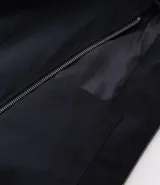 Campera masculina de corte boxy en color beige, con cuello inglés, cierre frontal de cremallera, mangas largas con puños elásticos y ruedo con elástico. Presenta bolsillos laterales y detalles de recortes en el diseño.