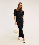 Pantalón negro de crepé con corte carrot, cintura alta con elástico en la parte trasera y lazo en la delantera, bolsillos delanteros con detalle metalizado y bolsillos cargo laterales.