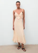 Vestido largo de estilo lencero en color beige, con escote de pico y detalles de encaje en el busto. Presenta tirantes finos, diseño evasé y forro interior.